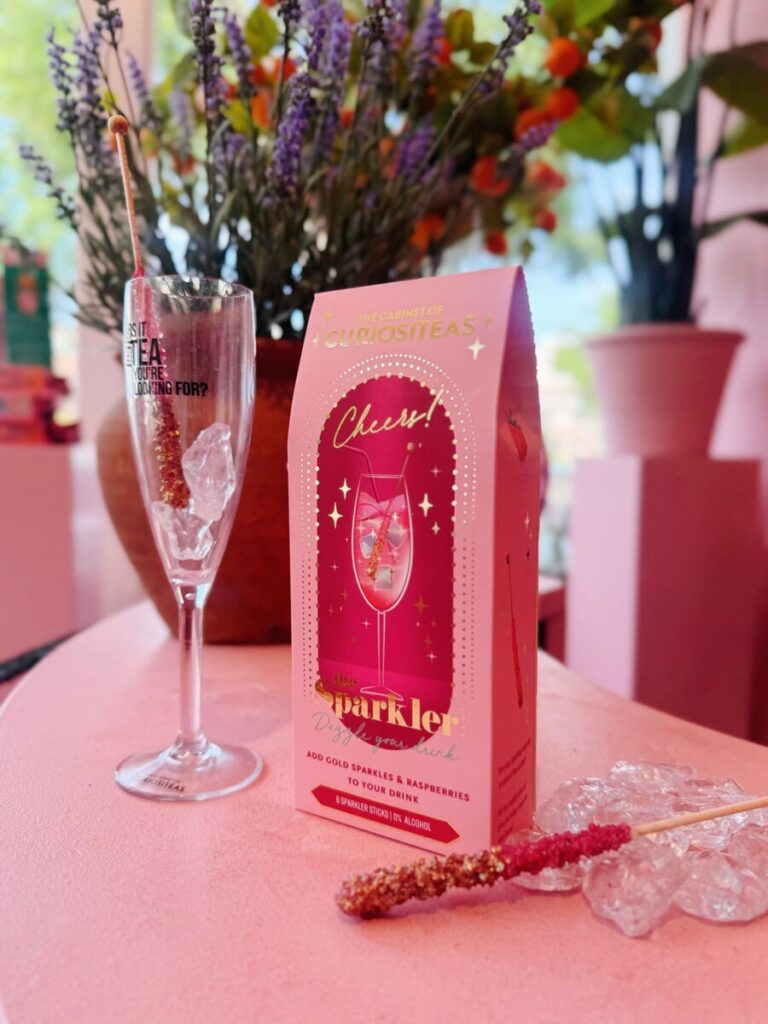 The Sparkler Mocktail Sticks met framboos en eetbare gouden glitters naast een champagneflute