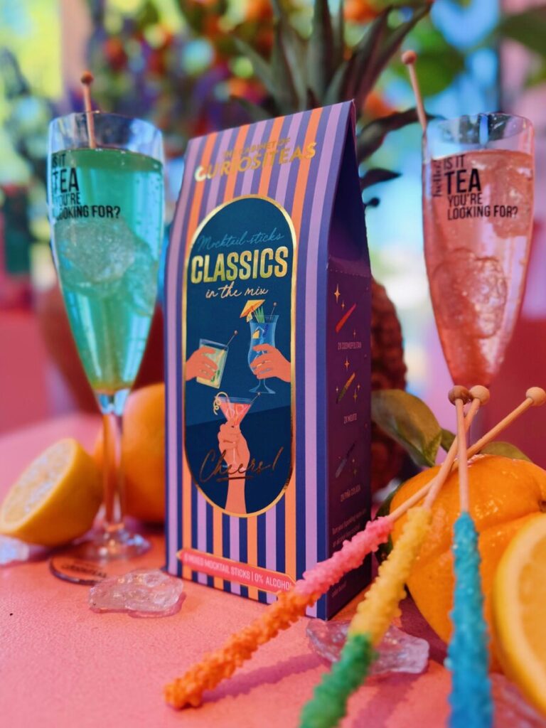 Mocktail Sticks Classics van Curiositeas met Cosmopolitan, Mojito en Piña Colada sticks naast twee champagneglazen met bruiswater